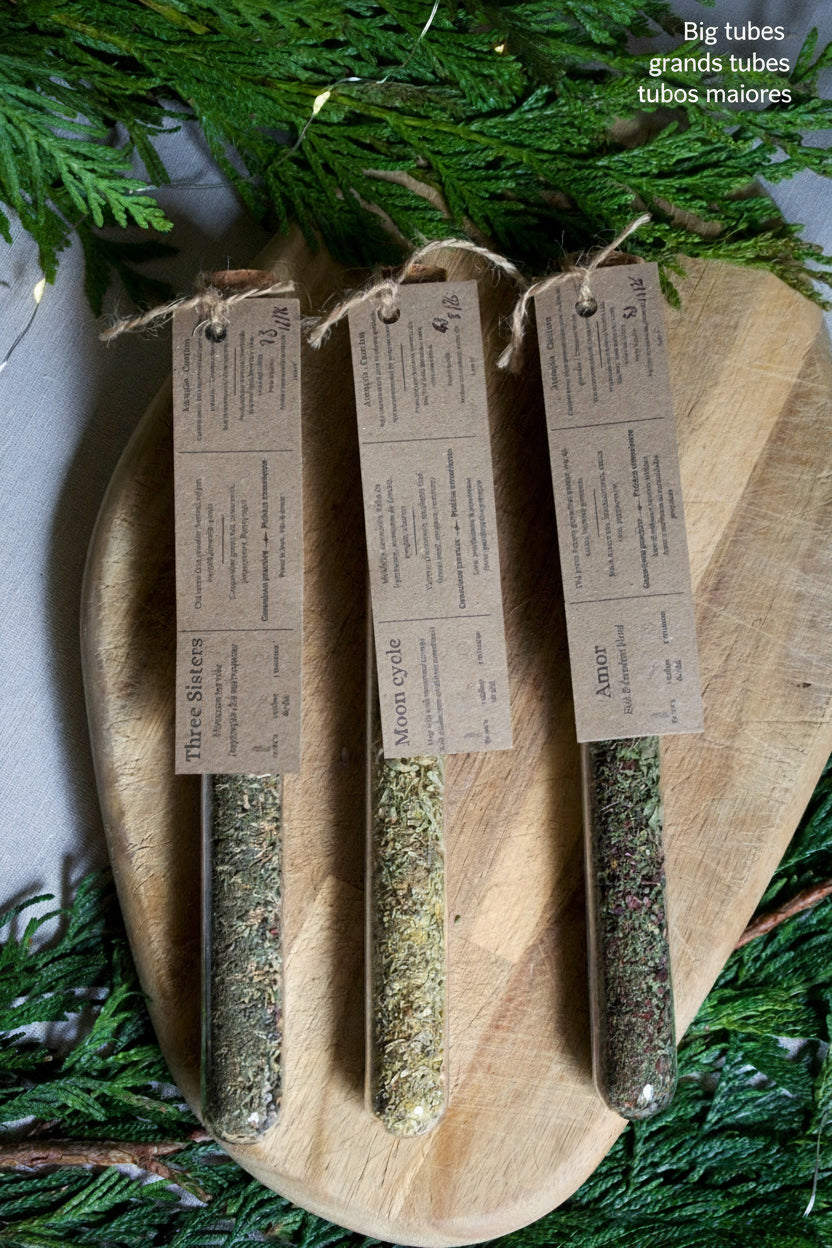 3 glass tubes containing teas and infusions, with their kraft label on top. On a wooden board and surrounded by greenery