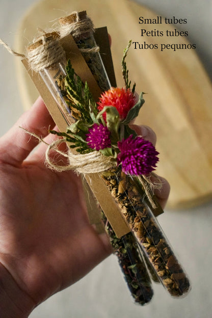 Bundle of three tubes held by a hand, tied together with a rope and some flowers. Background, wooden board and linen tablecloth.