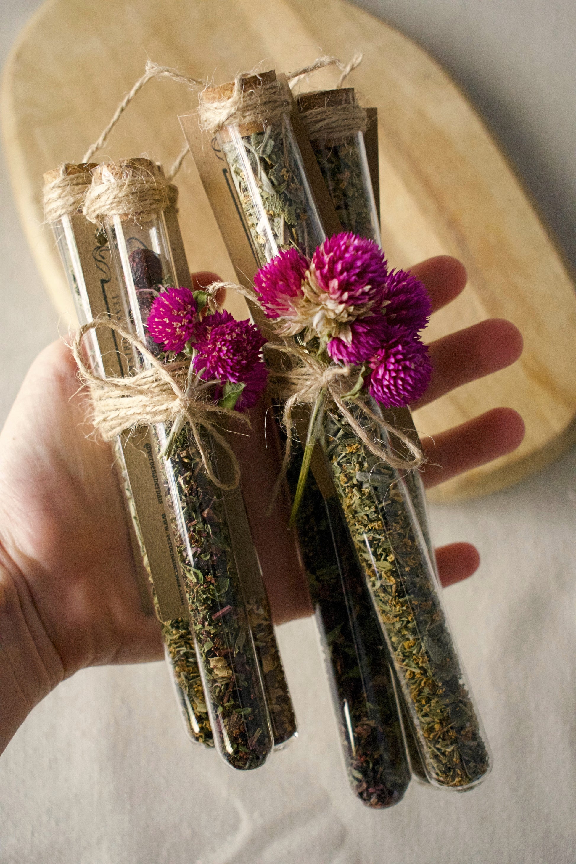 2 bundle of three tubes, small and regular tubes attached together with a rope and a flower for decoration. All filled in with different tea blends. Background: wooden board and linen tablecloth