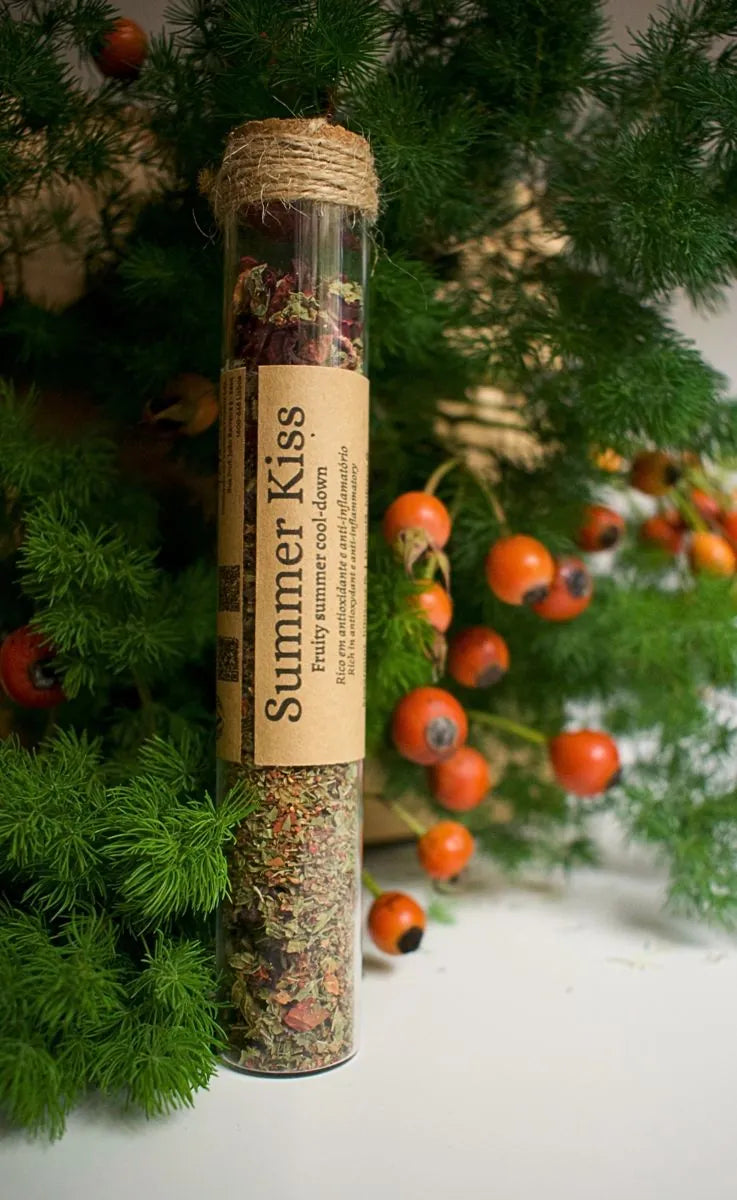 Glass tube with Summer kiss herbal blend, a kraft label is sticked on it with the information of the blend. Background is some greenery with rosebuds