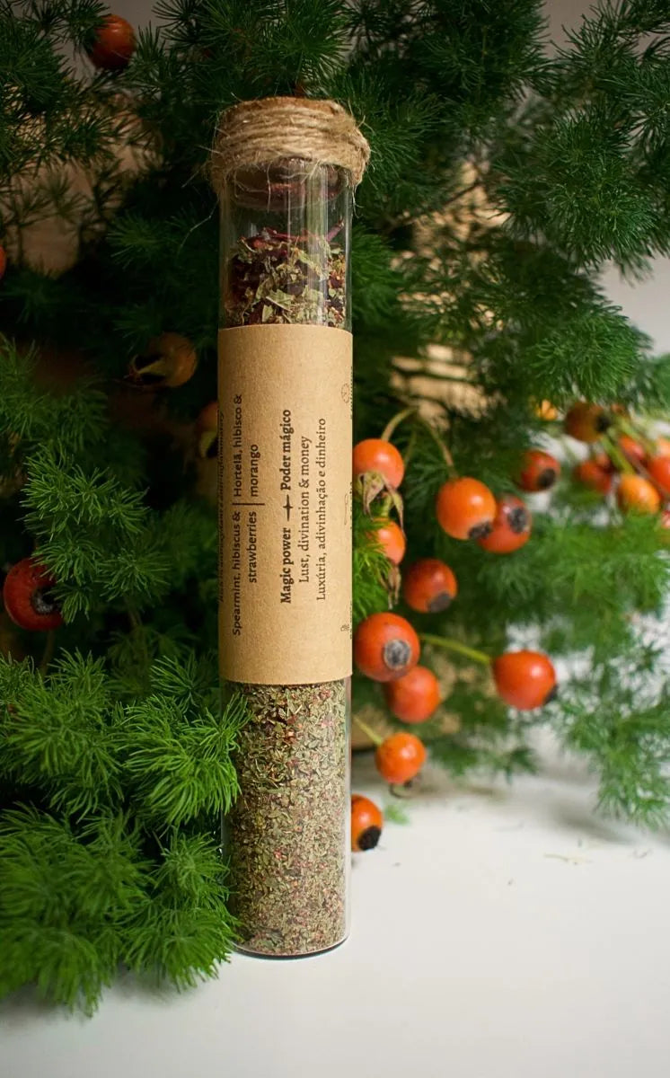 Glass tube with Summer kiss herbal blend, a kraft label is sticked on it with the information of the blend. Background is some greenery with rosebuds