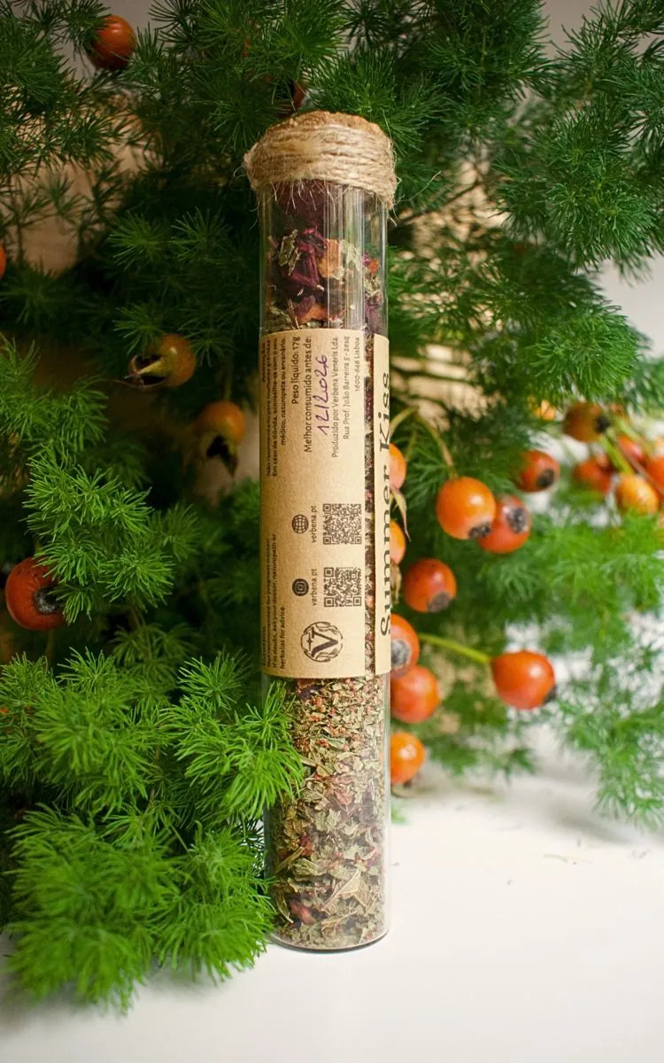 Glass tube with Summer kiss herbal blend, a kraft label is sticked on it with the information of the blend. Background is some greenery with rosebuds