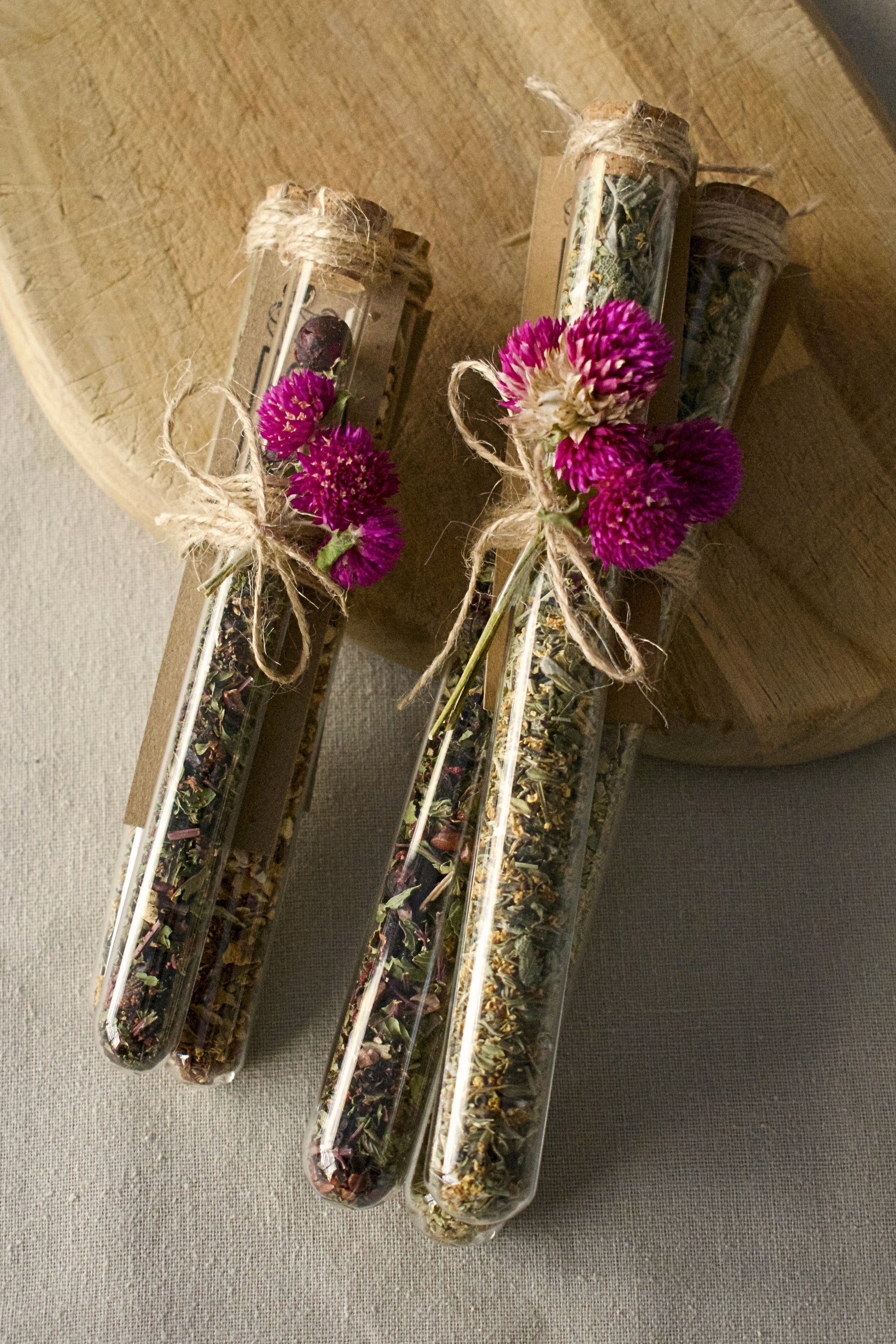 2 bundle of three tubes, small and regular tubes attached together with a rope and a flower for decoration. All filled in with different tea blends. Background: wooden board and linen tablecloth