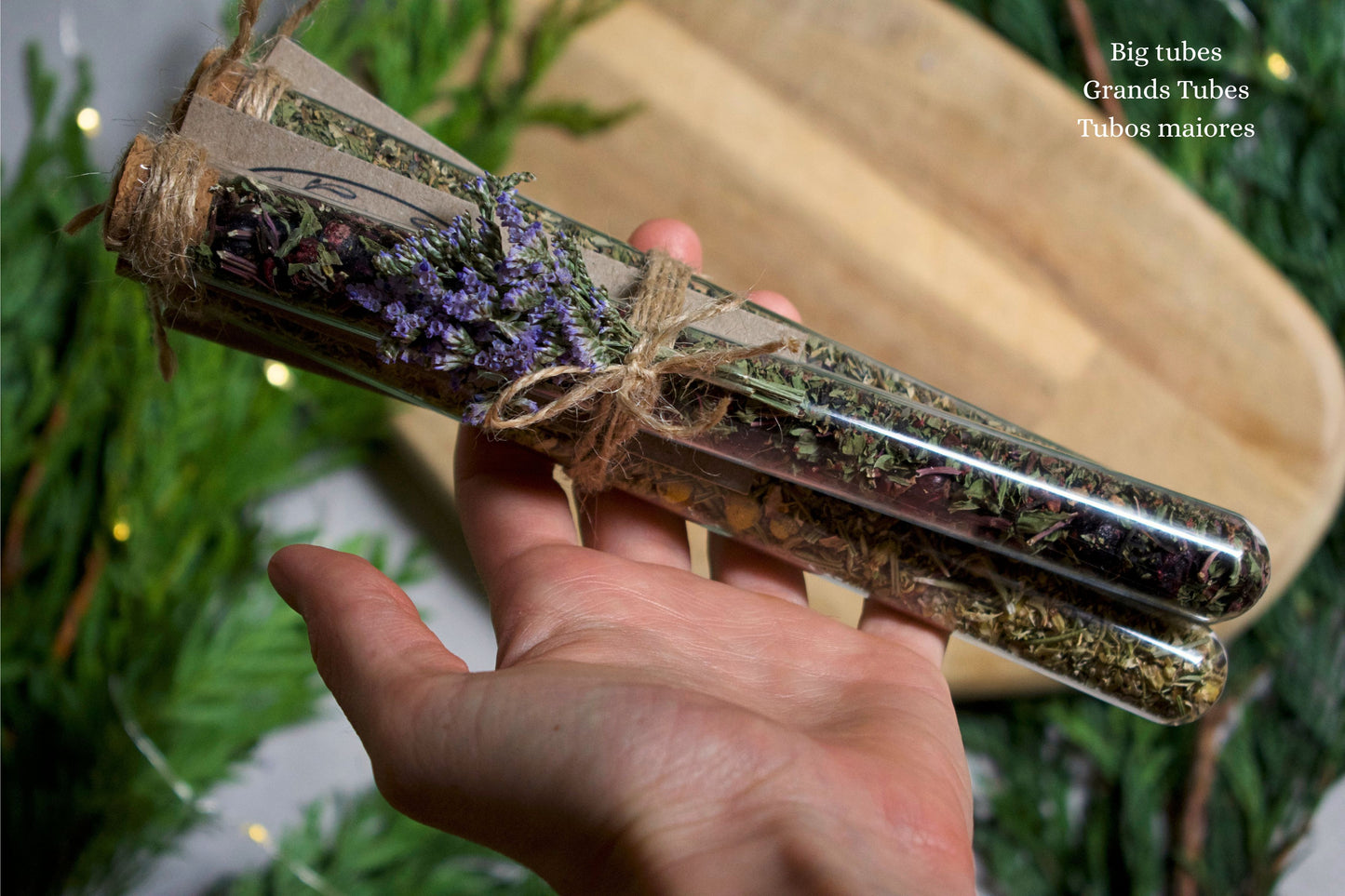 Hand holding, a bundle of three tubes with herbal blend inside. On the background we can see a wooden board and greenery.