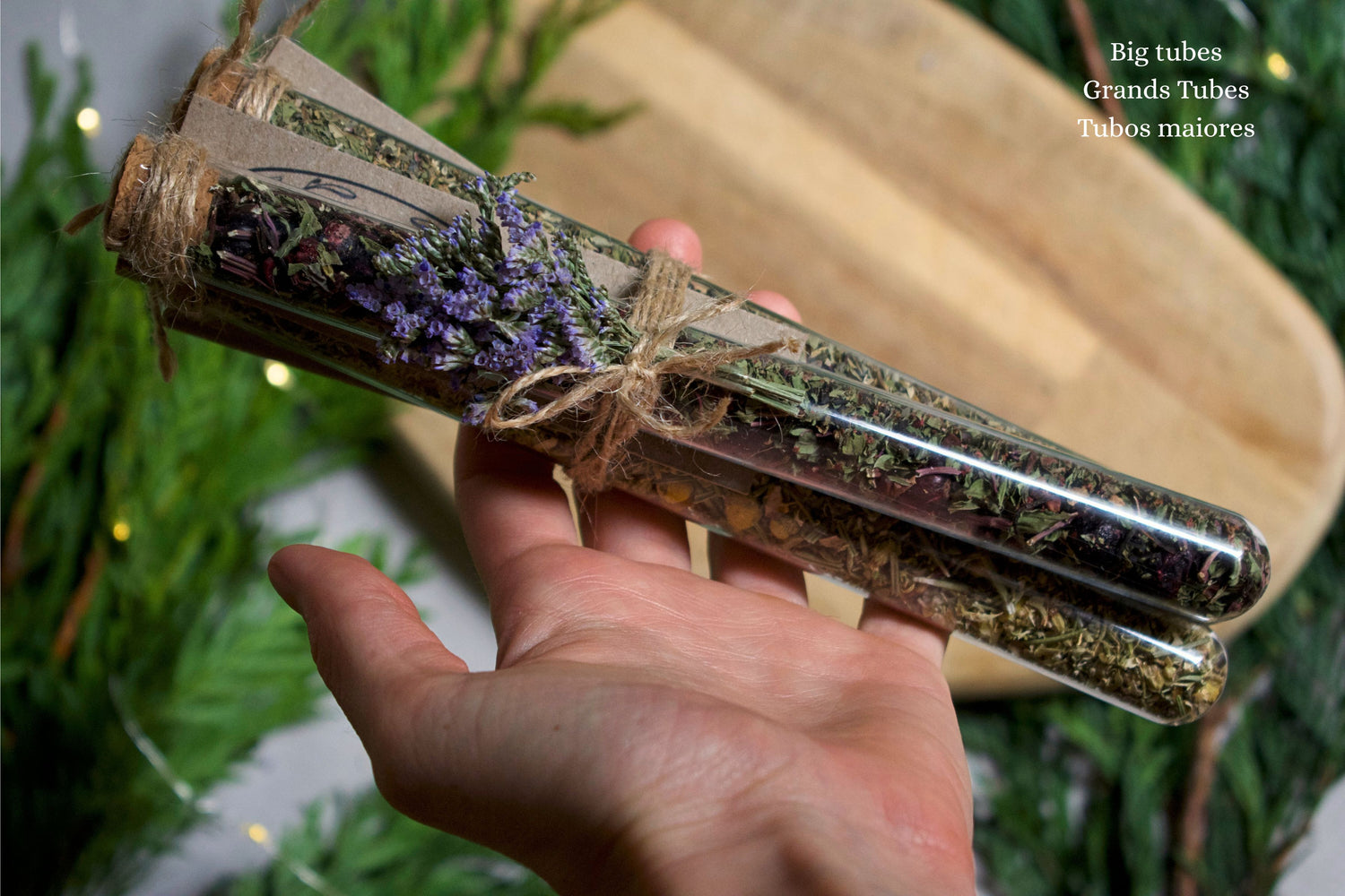Hand holding, a bundle of three tubes with herbal blend inside. On the background we can see a wooden board and greenery.